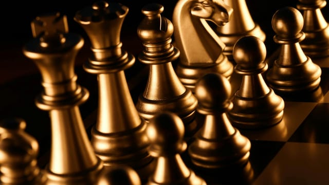 Close-up of shiny golden chess pieces on a checkered board. Symbolizes strategy and intelligence.