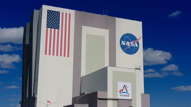 The iconic NASA Vehicle Assembly Building at Kennedy Space Center in bright daylight.