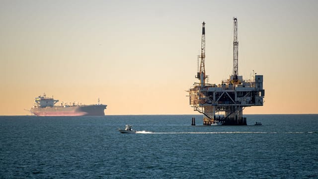 Offshore oil platform with container ship in tranquil sea during daytime.