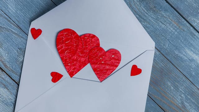 Close-up of a white envelope with red heart cutouts symbolizing romance and love.