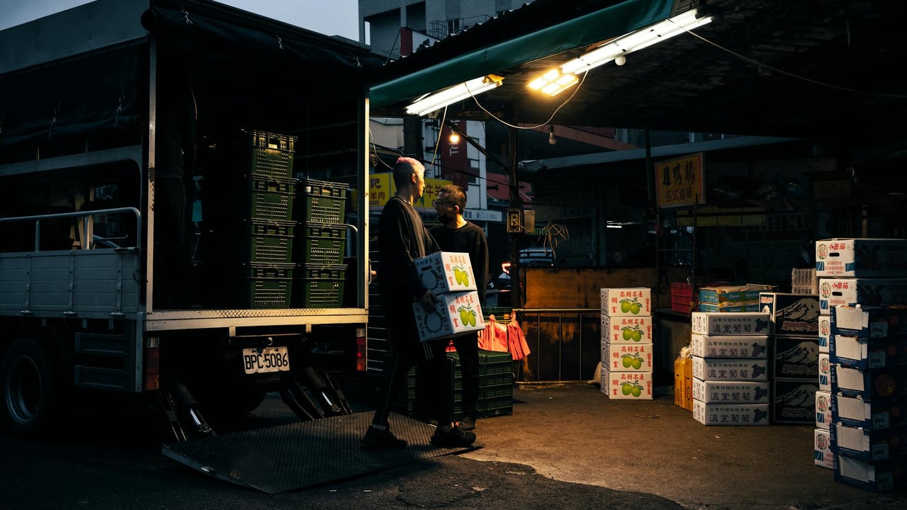 Workers unloading boxes from a delivery truck at an urban market during dusk.