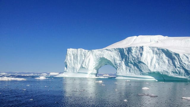 A stunning view of a large iceberg floating in the blue waters of Greenland, showcasing ice formations and global warming effects.