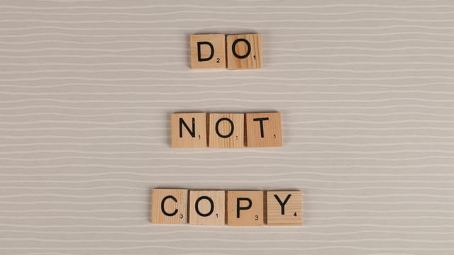 Close-up of wooden tiles spelling 'Do Not Copy' on a textured surface.