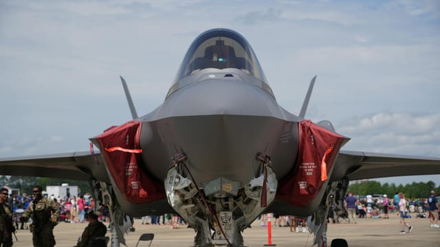 Front view of an F-35 fighter jet on display at an airshow in Hampton, Virginia with military personnel nearby.