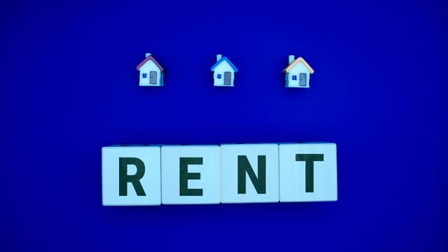 Miniature houses above letters spelling 'RENT' on a blue background, ideal for real estate themes.