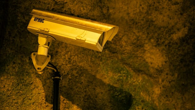 Close-up of a security camera mounted on a textured wall at night.