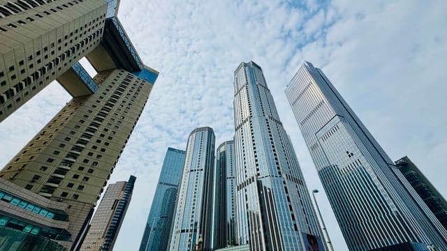 Low-angle view of modern skyscrapers in Tianjin under a partly cloudy blue sky.