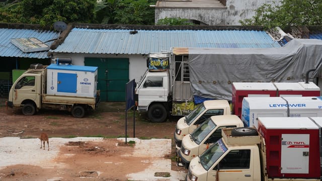 A row of parked utility trucks with generators beside a building outdoors.