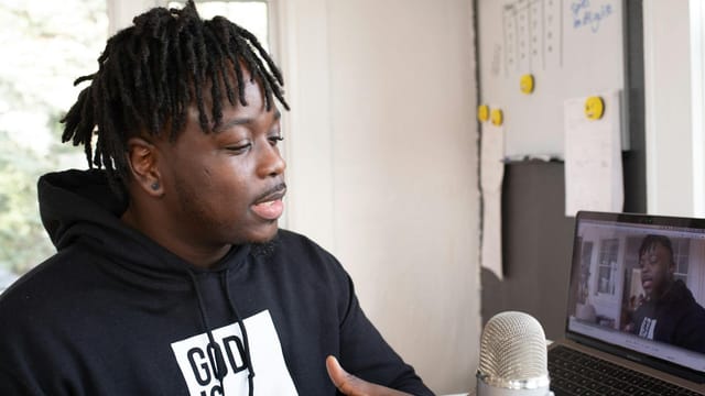 Man recording a podcast indoors with a laptop and microphone, focused and speaking.