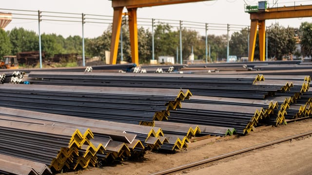 Numerous steel beams neatly stacked in an industrial yard during daytime.