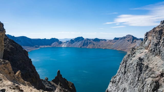 Dramatic landscape of Heaven Lake surrounded by rugged peaks under a clear blue sky.