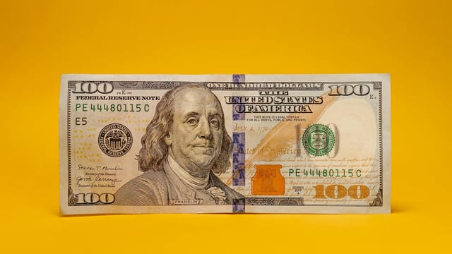 A close-up of a US hundred dollar bill on a warm yellow backdrop, ideal for financial themes.
