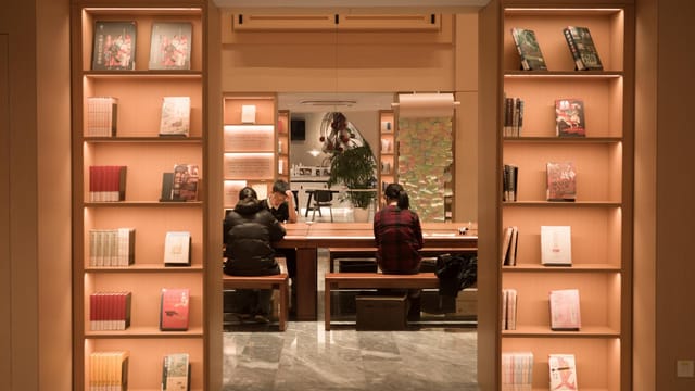 Cozy library interior in Shanghai featuring people reading at a table surrounded by illuminated bookshelves.