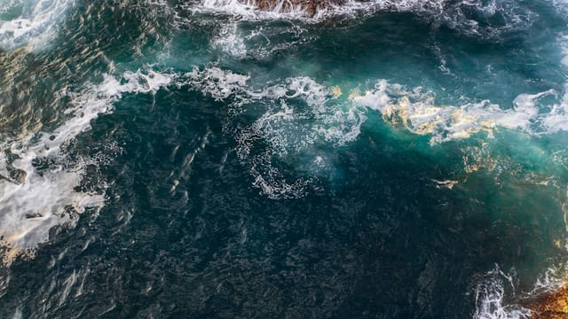 Dramatic aerial shot of ocean waves crashing against rocky shoreline, capturing the vibrant blue and white waters.