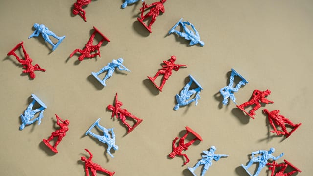 Red and blue toy soldiers arranged on a beige background, artistic flat lay.