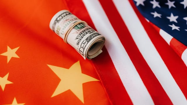 A rolled US dollar placed on overlapping USA and China flags, symbolizing international trade relations.