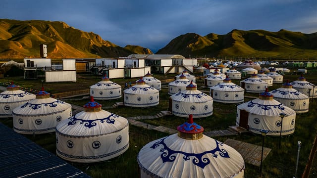 Aerial view of traditional yurts in a scenic mountain valley at sunset, showcasing nomadic lifestyle and natural beauty.