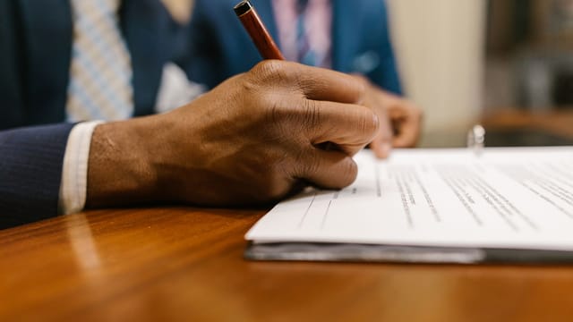 Close-up of an adult signing a legal document with a pen in an office.
