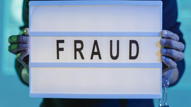 Close-up of hands holding a sign with 'fraud', illuminated in blue light.