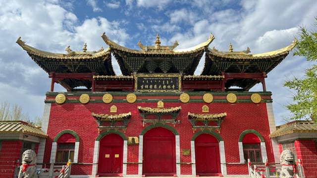 A vibrant red Chinese temple with intricate gold accents under a blue sky.