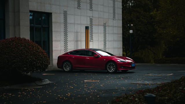 A sleek red electric car parked beside a modern building in an urban environment.