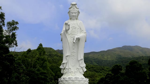 Stunning white Bodhisattva statue at Tsz Shan Monastery, Hong Kong, surrounded by lush greenery.