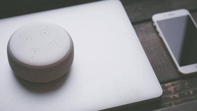 A smart speaker, laptop, and smartphone array representing modern technology lifestyle on a wooden surface.